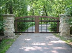 a gated driveway leading into a wooded area with stone pillars and gates on either side