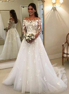 a woman standing in front of a mirror wearing a white wedding dress with long sleeves