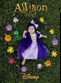 a baby is laying in the grass wearing a purple and white dress with flowers around it