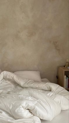 an unmade bed with white sheets and pillows