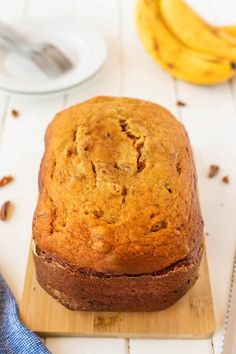 a loaf of banana bread sitting on top of a cutting board next to some bananas