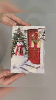 someone holding up a christmas card with a snowman in front of a red door