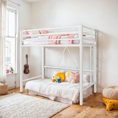 a white bunk bed sitting in a bedroom next to a wooden floor and window with pink pillows on it