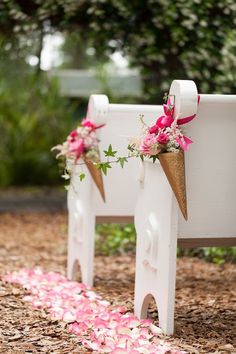 two white benches decorated with pink flowers and gold ribbon tied to the back of them