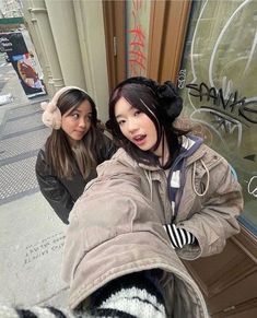 two young women standing next to each other in front of a store window with graffiti on it