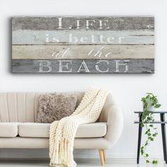 a living room with a white couch and wooden sign on the wall that says life is better at the beach