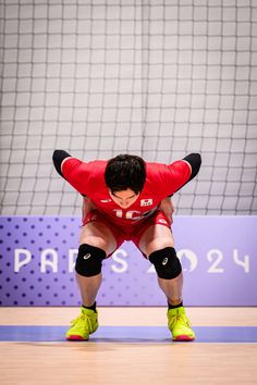 a man in red shirt and black shorts playing volleyball on court with net behind him