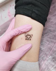 a person with pink gloves on their arm holding a small cat tattoo in her left hand