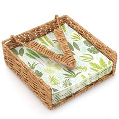 a wicker basket with green and white leaves on the bottom is holding two folded napkins