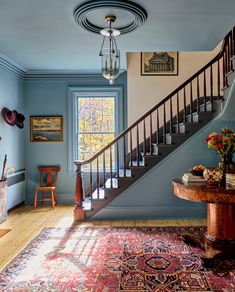 a room with blue walls and wooden floors has a red rug on the floor next to a stair case