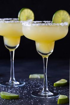 two margaritas with lime and salt garnish in coupe glasses on a black surface