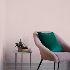 a chair with a green pillow on it next to a small table and potted plant