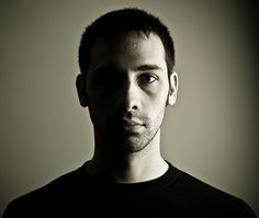 a black and white photo of a man in a dark t - shirt looking at the camera