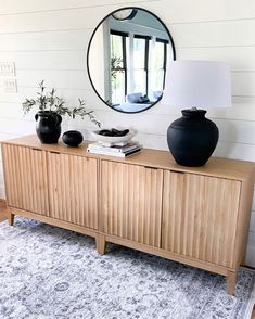 a wooden cabinet with two black vases on top of it next to a round mirror