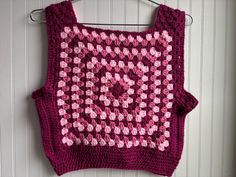 a crocheted sweater hanging on a wall with pink and white flowers in the center