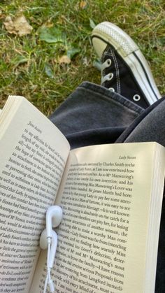 an open book with headphones attached to it sitting on the grass next to a pair of shoes