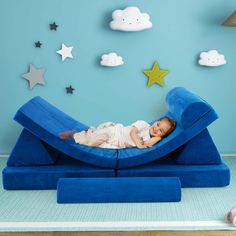 a baby laying on top of a blue couch in front of stars and clouds wall decals