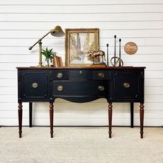 a black dresser with two drawers and a lamp on top, in front of a white wall