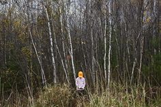 a woman standing in the middle of a forest with tall grass and trees behind her