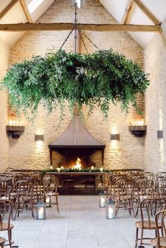 an indoor wedding venue set up with wooden chairs and greenery hanging from the ceiling