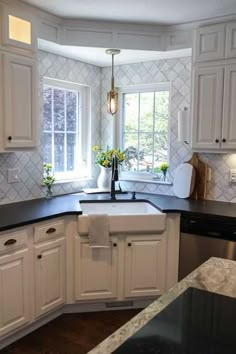 a kitchen with white cabinets and black counter tops in front of a window that has a potted plant on it