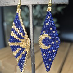 a pair of blue and gold beaded earrings sitting on top of a wooden table