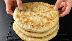 a stack of flat breads being held by two hands over a cooling rack on a black surface