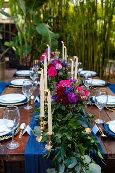 the table is set with blue linens, candles and colorful flowers in vases