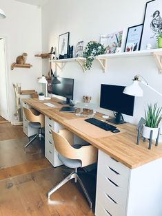 a desk with two computer monitors on top of it next to a lamp and shelves