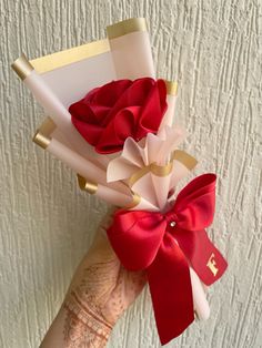 a woman's hand holding some red and white paper with a bow on it