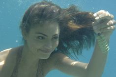 a woman is under the water holding her hair in one hand and looking at the camera