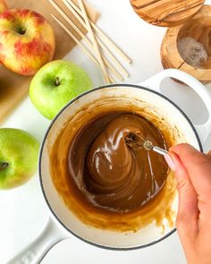 a person is dipping some kind of chocolate in an apple bowl next to other apples