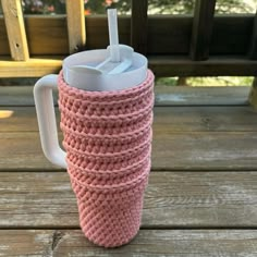 a pink knitted coffee cup with a straw in it sitting on a wooden table