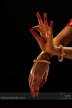 two hands with red nail polish and gold bracelets