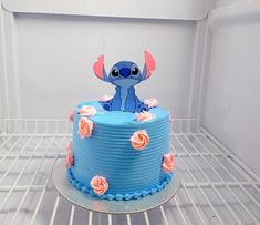 there is a blue cake with pink flowers on the bottom and an image of stitch