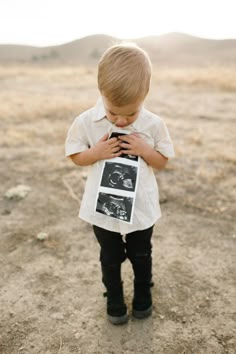 a little boy standing in the dirt holding a cell phone