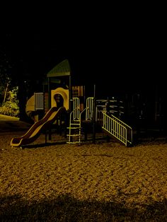 a child's play area at night with a slide and climbing frame in the background