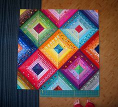 someone is standing on the floor next to a colorful patchwork quilt that has been made into a square