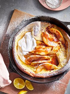 a cast iron skillet filled with food on top of a wooden cutting board next to sliced lemons