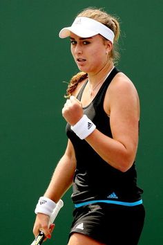 a woman holding a tennis racquet on top of a tennis court in front of a green wall