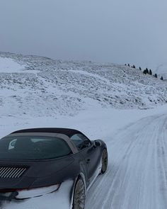 a black sports car driving down a snow covered road in the middle of an open field