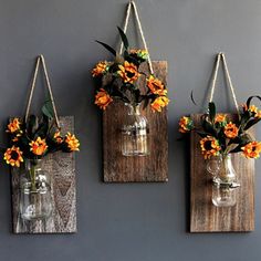 three hanging mason jars with flowers in them on a wall next to a gray wall