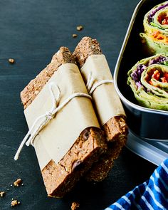 two pieces of bread wrapped in brown paper next to a bowl of guacamole