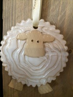 a ceramic sheep ornament hanging on a wooden wall with a white ribbon around it