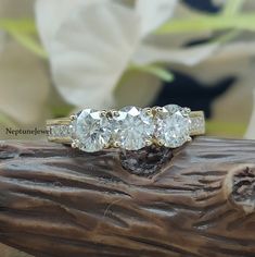 three stone diamond ring sitting on top of a piece of wood with flowers in the background