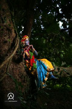 a woman with painted face and body sitting on a tree branch in the forest, wearing an elaborate headdress