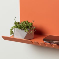 an orange shelf with a potted plant and cell phone on it next to the wall