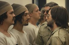 a group of men standing next to each other in front of a mirror with one man wearing glasses