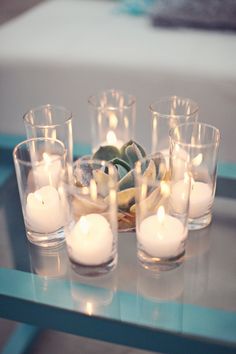 candles are arranged on a glass table with succulents