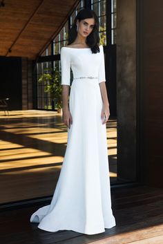 a woman standing in front of a door wearing a white dress with sleeves and beaded belt